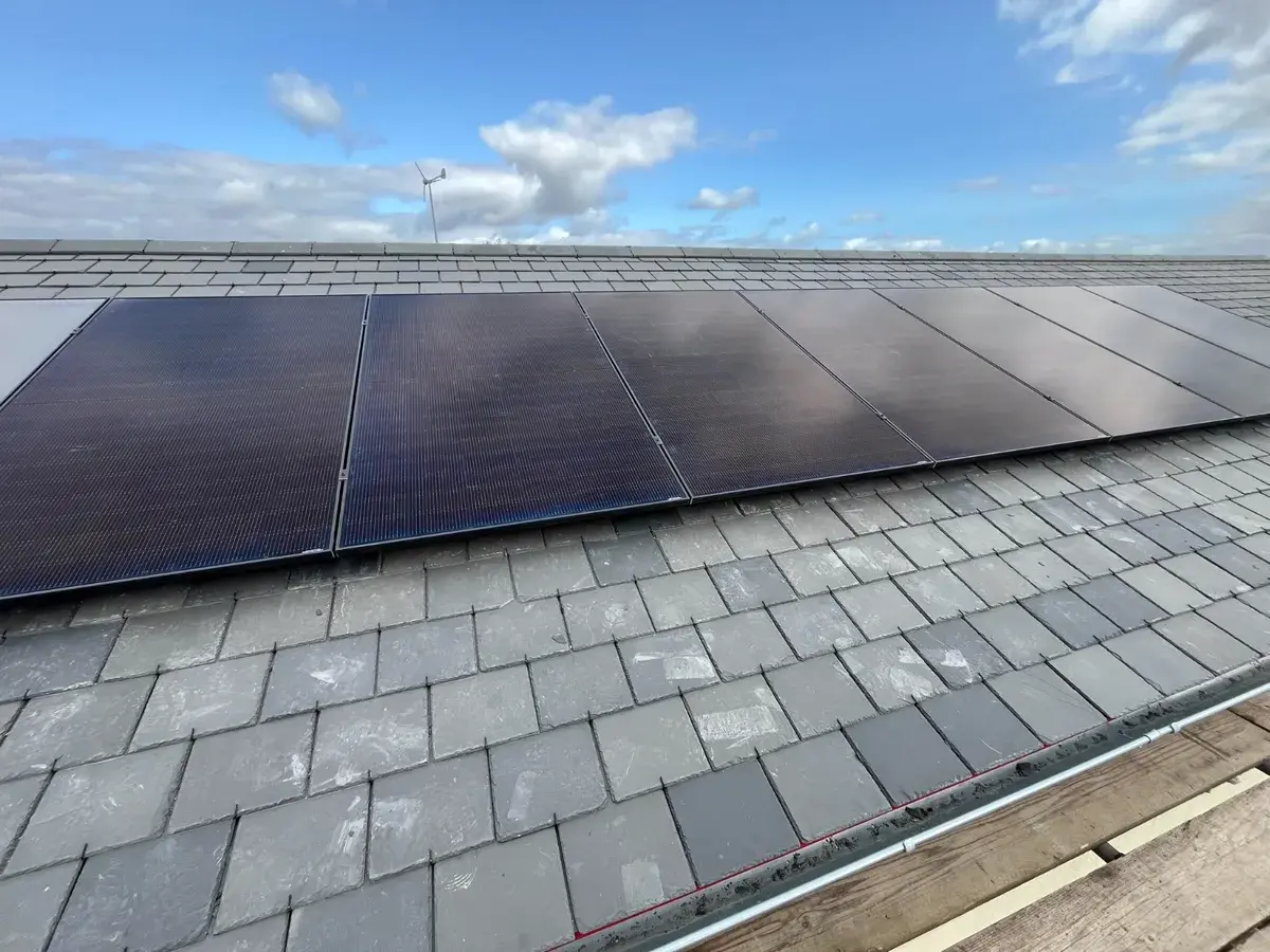 On-roof solar panels on slate with blue sky and wind turbine