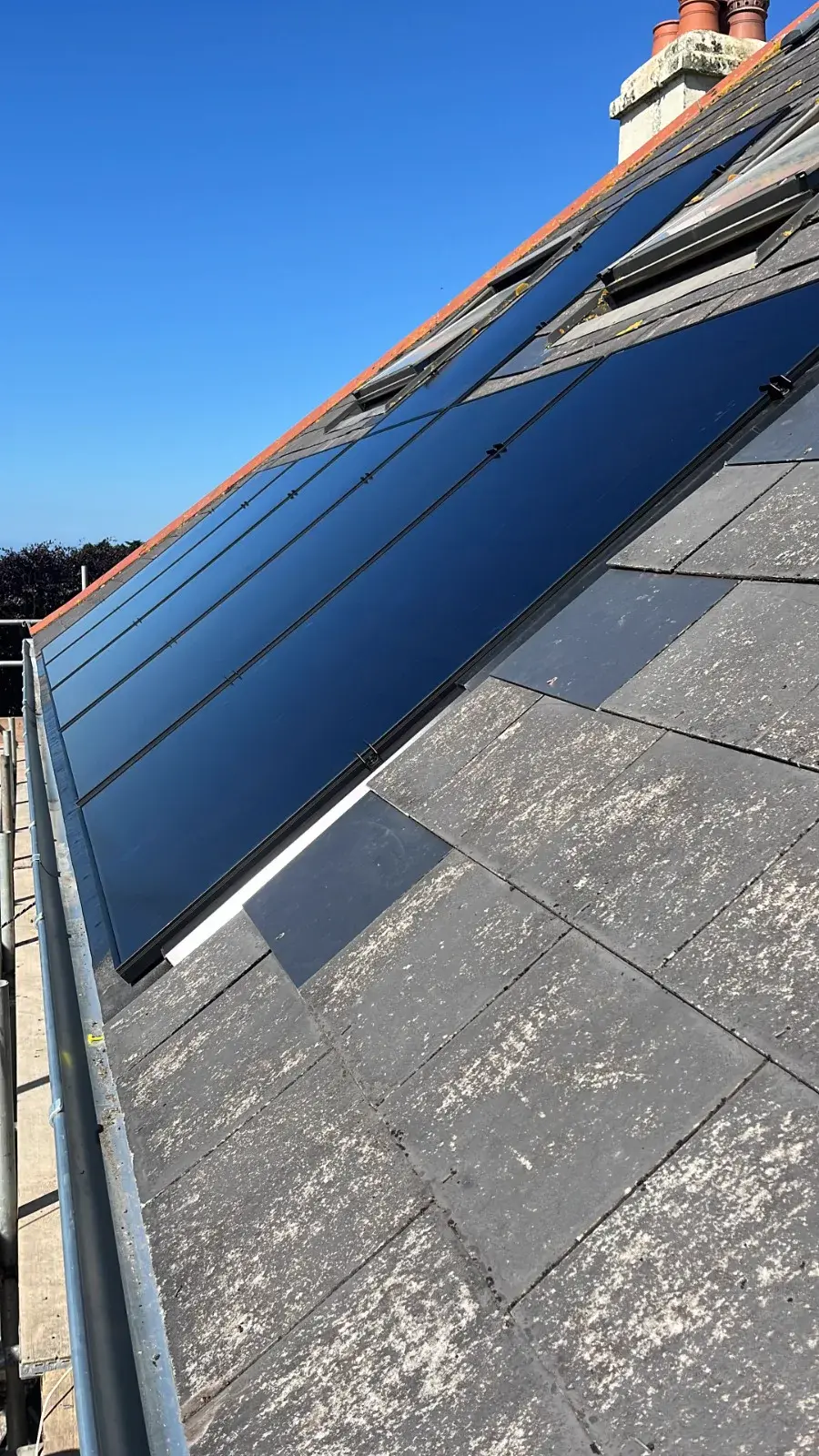 All-black solar panels installed on slate roof, blue sky