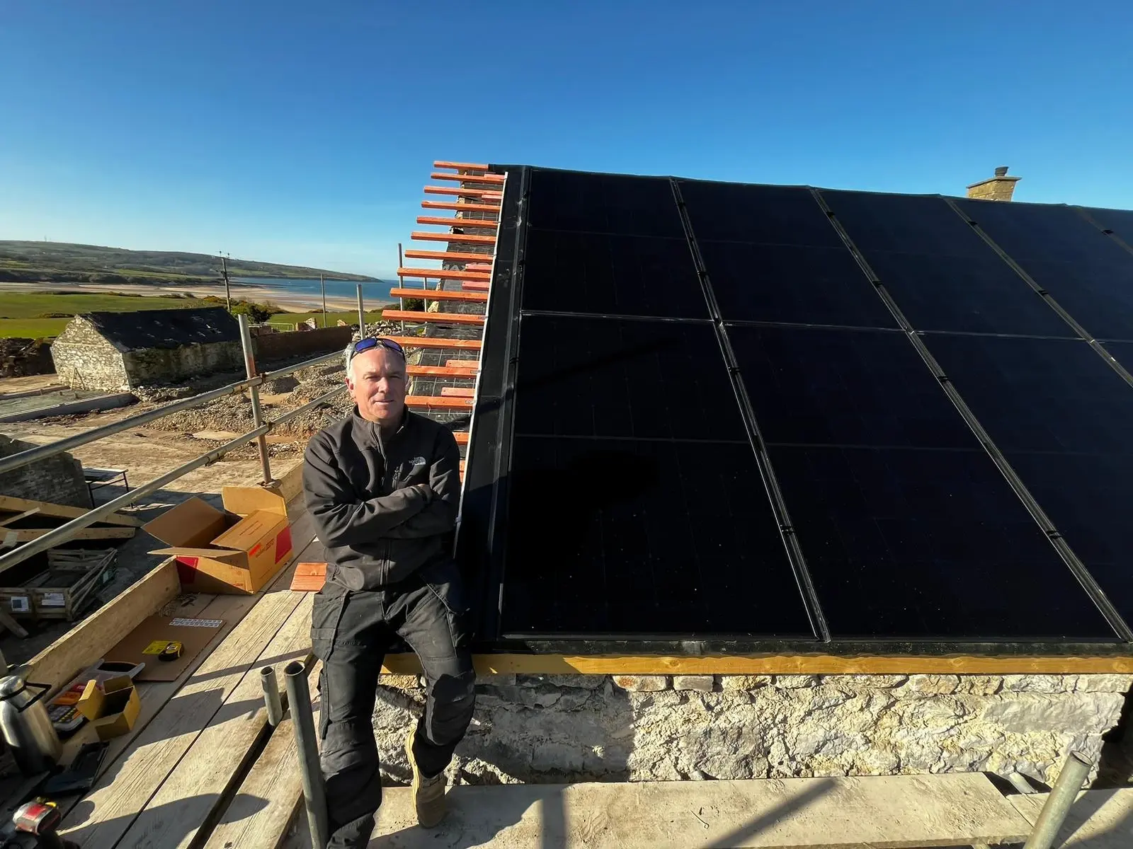 Matt on scaffolding beside completed in-roof solar panels overlooking coast