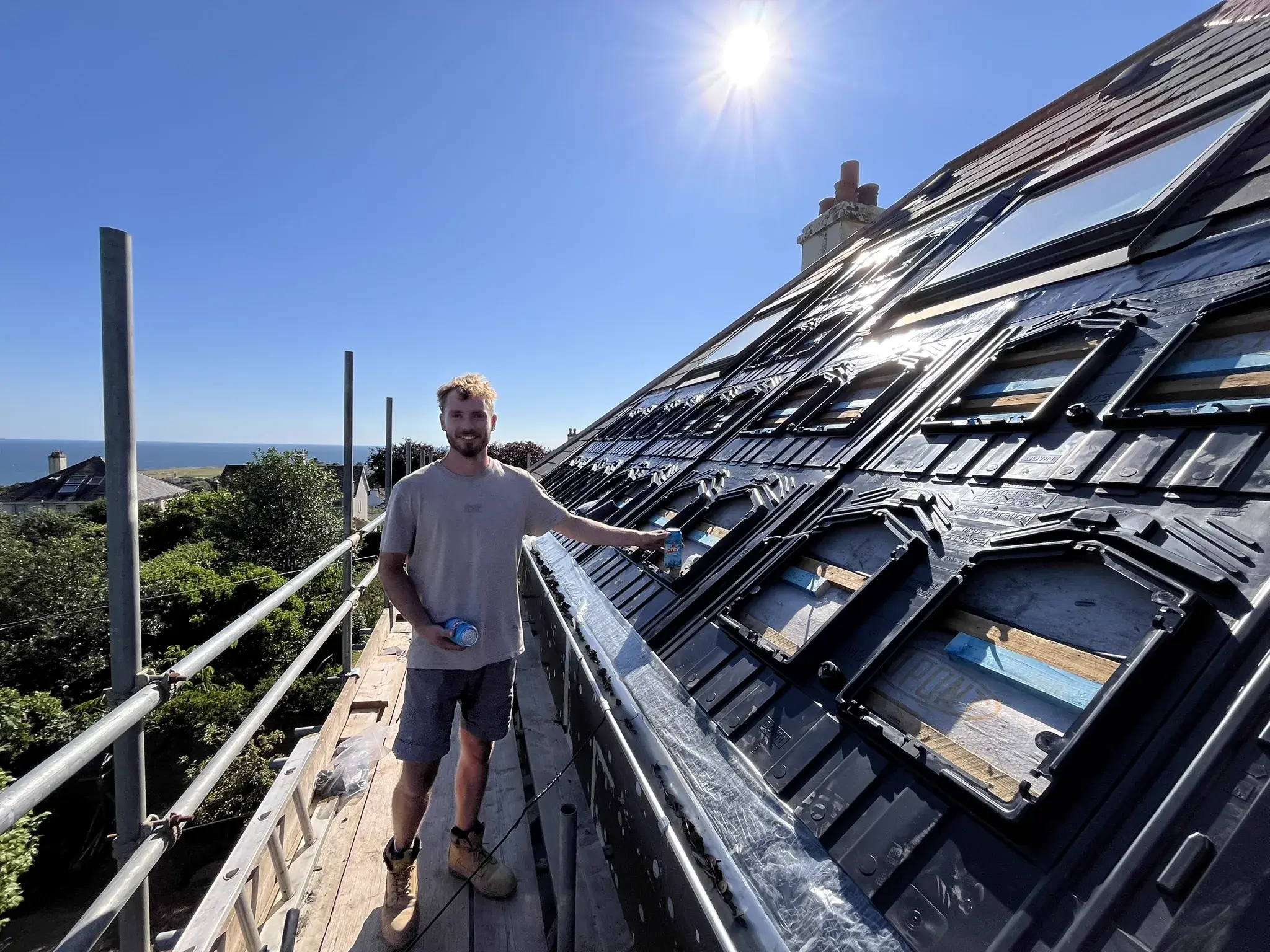 Installer on scaffolding fitting solar panels with sea view behind