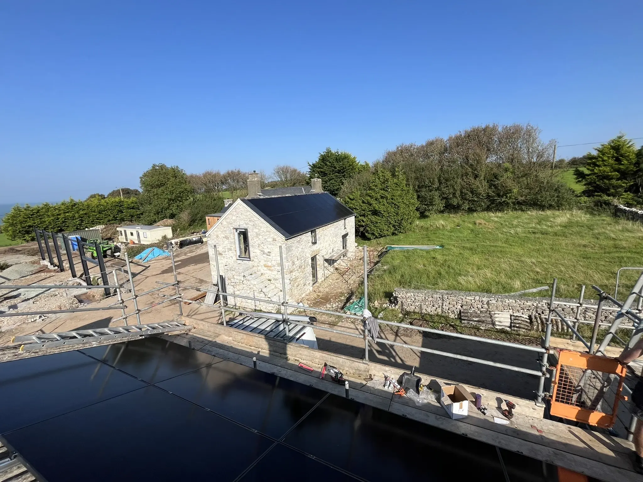 View from scaffolding over solar panels to stone outbuilding and coast